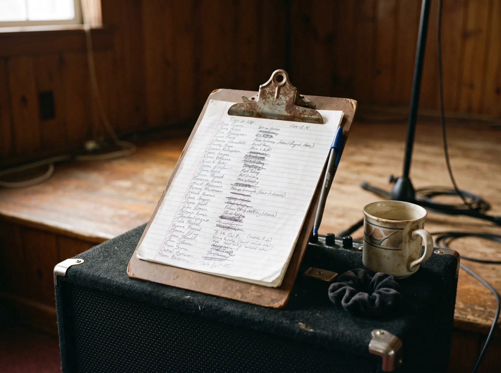 A worn brown clipboard with a handwritten sign-up sheet resting on a bass amplifier